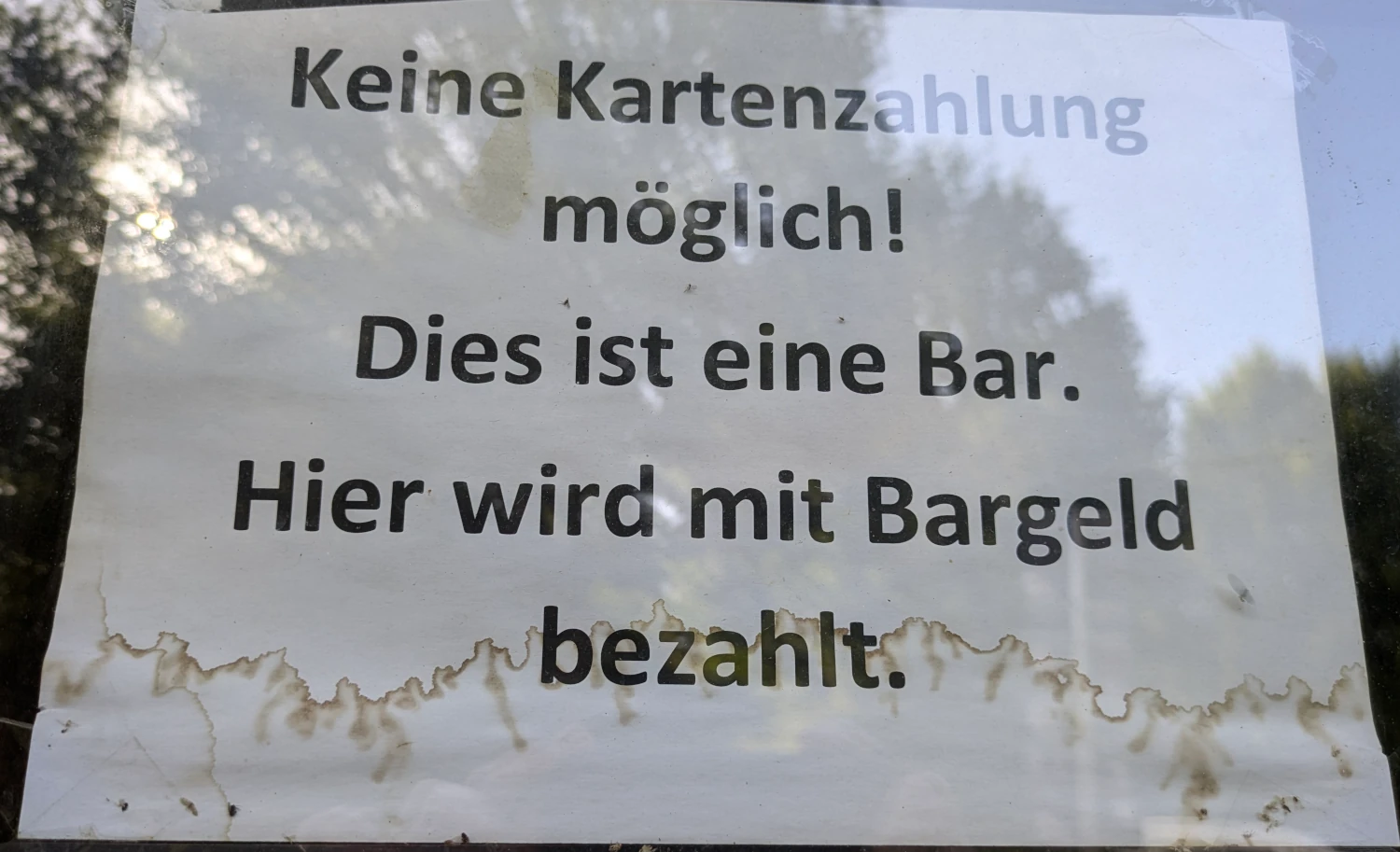 Ein Schild hinter einem Fenster mit der Aufschrift: Keine Kartenzahlung möglich! Dies ist eine Bar. Hier wird mit Bargeld bezahlt.