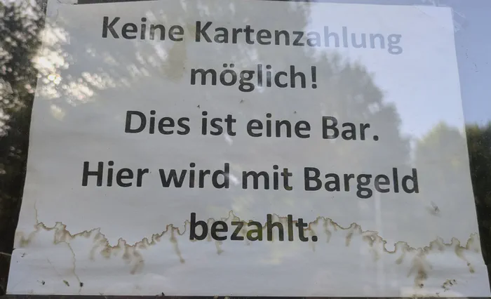 Ein Schild hinter einem Fenster mit der Aufschrift: Keine Kartenzahlung möglich! Dies ist eine Bar. Hier wird mit Bargeld bezahlt.